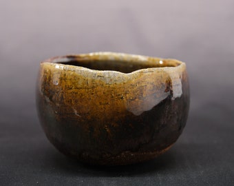 May include: A brown and black ceramic bowl with a rough, textured surface. The bowl has a wide, rounded shape and a slightly uneven rim.