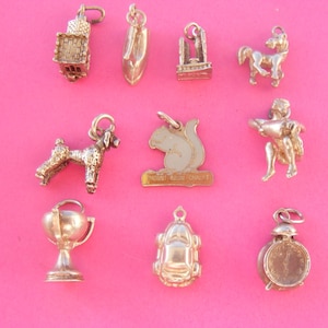 May include: A selection of silver charms, featuring a castle, a shoe, a well, a horse, a poodle, a squirrel, a cherub, a trophy, a car, and a clock. The charms are set against a pink backdrop.