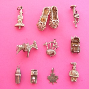 Puede incluir: Colección de dijes plateados sobre fondo rosa. Los dijes incluyen una figura, zapatillas de ballet, una trompeta, un burro, gaitas, una gramola, una coctelera, una cafetera, una hoja de arce y un chef.
