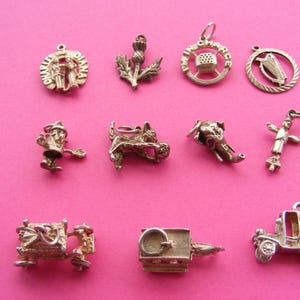 Può includere: Una collezione di ciondoli vintage in argento, tra cui un cardo, un'arpa, una carrozza e una figura con un cappello. I ciondoli sono esposti su uno sfondo rosa acceso. I ciondoli sono piccoli e dettagliati.