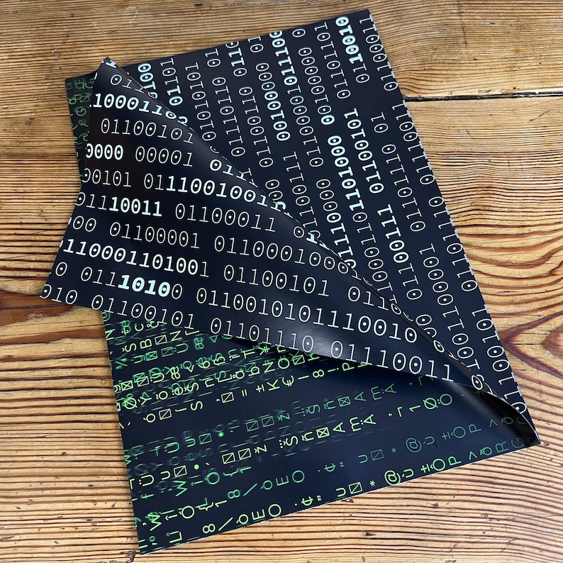 以下が含まれることがあります： 白いバイナリコードの繰り返しパターンが施された黒い包装紙。紙が折り畳まれ、緑と黒のパターンがさまざまな記号と文字で明らかになっている。