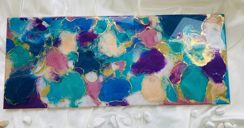 Puede incluir: Obra de arte abstracta rectangular con acabado brillante. La obra presenta una vibrante mezcla de colores, incluyendo turquesa, azul, morado, rosa y dorado. El dise&ntilde;o incorpora formas org&aacute;nicas y patrones fluidos.