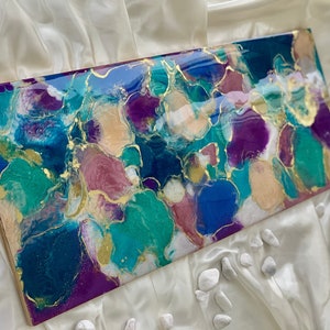 Puede incluir: Obra de arte abstracta rectangular con acabado brillante. La obra presenta una mezcla de colores turquesa, morado, azul y dorado. El dise&ntilde;o incluye formas org&aacute;nicas y detalles dorados, creando una est&eacute;tica moderna.