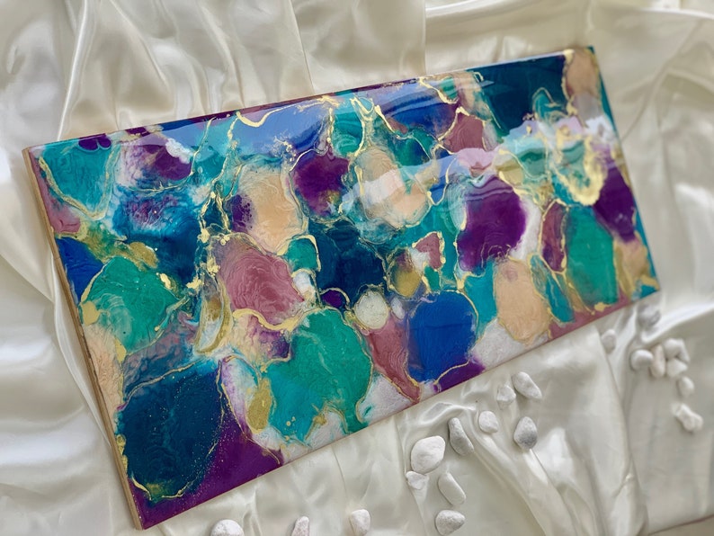 Puede incluir: Obra de arte abstracta rectangular con acabado brillante. La obra presenta una mezcla de colores turquesa, morado, azul y dorado. El dise&ntilde;o incluye formas org&aacute;nicas y detalles dorados, creando una est&eacute;tica moderna.