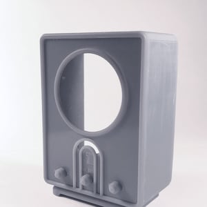 May include: A grey plastic model of a vintage television set with a round screen and a speaker grill. The model has a label that reads "VE 391".