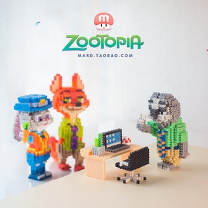 Puede incluir: Un colorido diorama con personajes de la película "Zootrópolis" construido con pequeños bloques de construcción. La escena incluye a Judy Hopps, Nick Wilde y otros personajes en un escritorio con una computadora. El texto "Zootopia" y "MARD.TAOBAO.COM" son visibles.