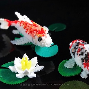 Może przedstawiać: Szczegółowy obraz miniaturowej sceny stawu z dwoma karpiami koi i lilią wodną, ​​wszystkie zbudowane z małych, kolorowych klocków. Karpie koi są białe z czerwonymi i czarnymi oznaczeniami. Lilia wodna ma białe płatki i żółty środek.