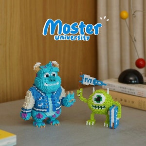 Peut inclure: Deux figurines pixélisées de Monstres et Cie. L'une est un grand monstre bleu portant une veste de collège. L'autre est un petit monstre vert tenant un drapeau et un livre. Le texte "Monster University" est au-dessus.
