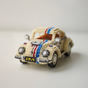 May include: A cream-colored toy car, constructed from small, colorful beads. The car features a racing stripe in red, white, and blue, with the number "53" on the hood. The car has black tires and a license plate.