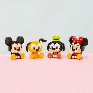 Puede incluir: Cuatro figuras de bloques de colores de los personajes de Disney Mickey Mouse, Pluto, Goofy y Minnie Mouse. Mickey tiene orejas negras y un atuendo amarillo. Pluto es amarillo. Goofy tiene un sombrero verde y pantalones naranjas. Minnie tiene un lazo y un vestido rojos.