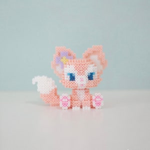 Puede incluir: Una figura de zorro pixelada hecha a mano en tonos rosa, blanco y azul. El zorro tiene ojos azules, un hocico blanco y una cola blanca y esponjosa. Está adornado con un lazo morado y una flor amarilla. La figura está hecha de pequeñas cuentas de colores.
