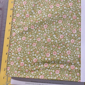 May include: A floral patterned fabric in shades of green, white, and peach. The fabric is folded and resting on a yellow surface with a ruler. The text on the paper says "Machine Wash Cold. Tumble Dry Low. Remove Immediately."