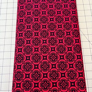 May include: Red fabric with a black repeating pattern of stylised flowers and circles.
