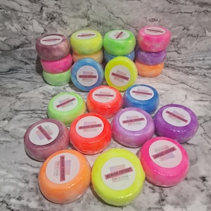May include: A selection of brightly coloured bath bombs, including pink, purple, orange, yellow, green, and blue. Each round bomb is wrapped in clear plastic and features a circular label with the text "HEAVEN ESSENCE HOME & SPIRIT".