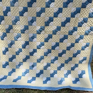 May include: A blue and yellow patchwork quilt with a geometric pattern. The quilt is made of squares and rectangles of different sizes and colors. The quilt is edged with a blue border.