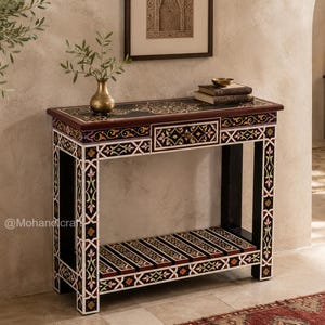 Peut inclure: Une console rectangulaire en bois avec une finition sombre et des motifs floraux et géométriques incrustés en blanc, or et multicolore. La table comprend un tiroir central unique et une étagère inférieure à lattes, marquée @Mohandcraft.