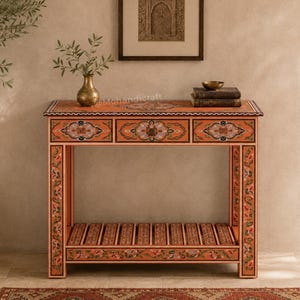 May include: A rectangular console table with a burnt orange finish, featuring intricate floral patterns in white, green, and black. The table has three drawers across the top, a slatted lower shelf, and four straight legs, with the text Mohandicraft visible.