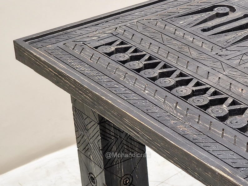May include: Close-up of a dark stained wooden table with intricate carved geometric patterns. The table has a rectangular top and a sturdy leg, showcasing detailed craftsmanship. The design includes circles and linear elements.