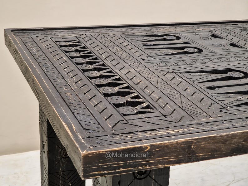 May include: A dark brown wooden table with detailed carved geometric patterns. The table's surface features a design of lines, circles, and shapes, creating a textured appearance. The table's legs are visible, matching the dark brown colour and carved design.