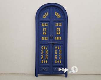Op de afbeelding: Een blauwe dubbele deur met gele gegraveerde details. De deur heeft een traditioneel Marokkaans ontwerp met een gebogen bovenkant en ingewikkelde gravures.