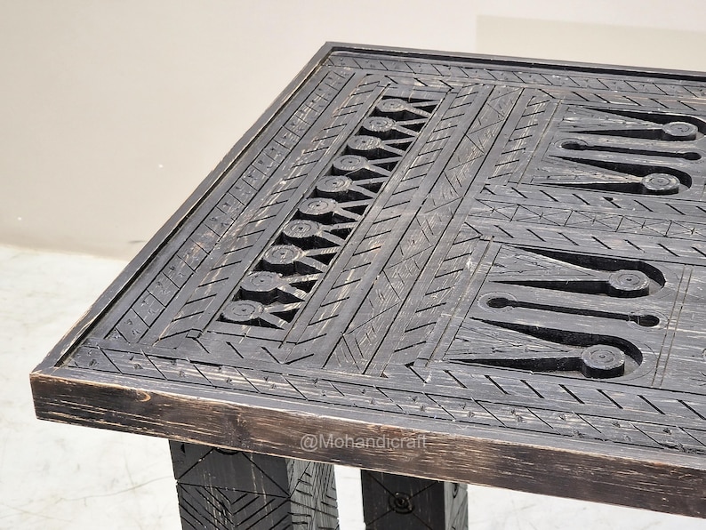 May include: A dark-stained wooden table with detailed carved geometric patterns. The rectangular tabletop features intricate designs, including circles, triangles, and linear elements. The table's legs are also carved, giving a rustic, handcrafted appearance.
