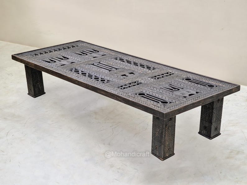 May include: A dark-stained wooden coffee table with a rectangular top featuring detailed carved geometric designs. The table has four square legs, and the design suggests a handcrafted origin. The table is approximately 122 cm long.