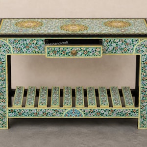 May include: A rectangular console table featuring a light green base with intricate floral patterns in blue, red, and white. The table includes a single central drawer with a small round knob and a slatted lower shelf. The text Mohandicraft is visible.