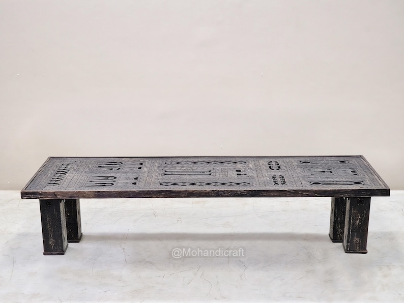 May include: Dark brown rectangular coffee table with carved geometric patterns and text. The table has four sturdy, dark brown legs. The table is approximately 152 cm long, 51 cm wide, and 41 cm high.