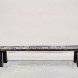 May include: A dark brown rectangular coffee table with a patterned top and four sturdy legs. The table is made of wood and has a rustic, aged appearance. The table is approximately 152 cm long.