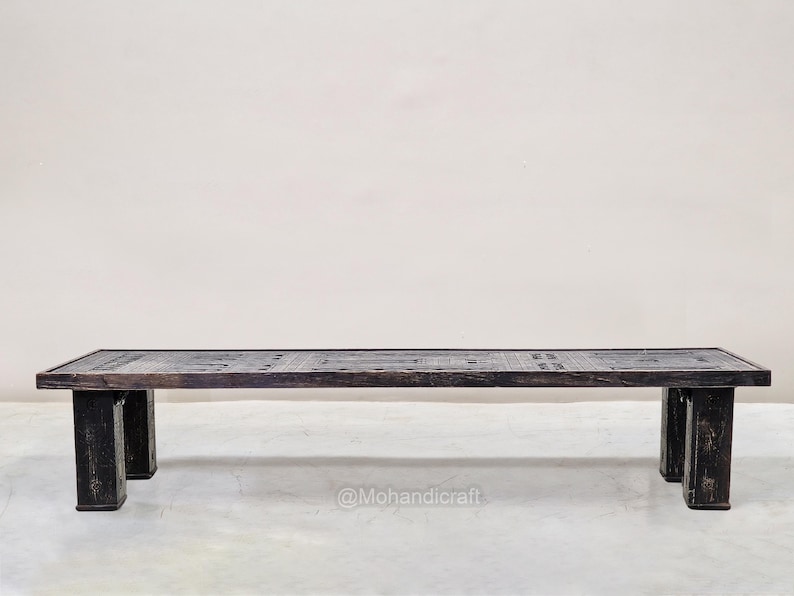 May include: A dark brown rectangular coffee table with a patterned top and four sturdy legs. The table is made of wood and has a rustic, aged appearance. The table is approximately 152 cm long.