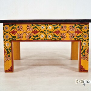 May include: A small, hand-painted wooden table with a black top and yellow sides. The sides are decorated with a floral pattern in red, green, and pink. The table is approximately 12 inches long, 8 inches wide, and 6 inches high.