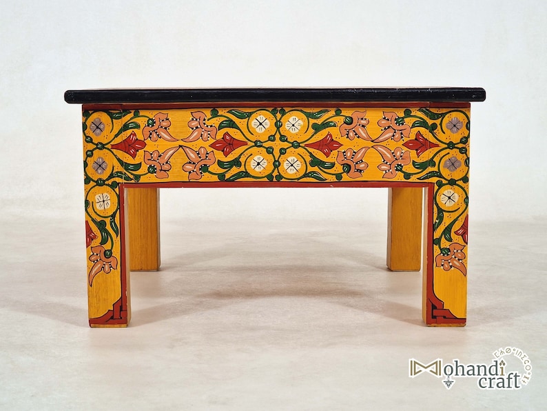 May include: A small, hand-painted wooden table with a black top and yellow sides. The sides are decorated with a floral pattern in red, green, and pink. The table is approximately 12 inches long, 8 inches wide, and 6 inches high.