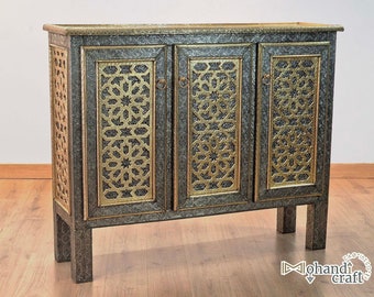 May include: A three-door cabinet with intricate gold and black geometric patterns on each door. The cabinet has a dark wood finish and sits on four legs.