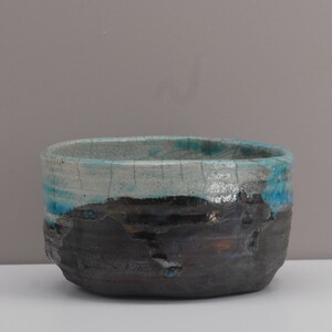 Puede incluir: Un cuenco de cer&aacute;mica con un esmalte blanco y detalles azules y negros. El cuenco tiene un esmalte craquelado y una superficie rugosa y texturizada.