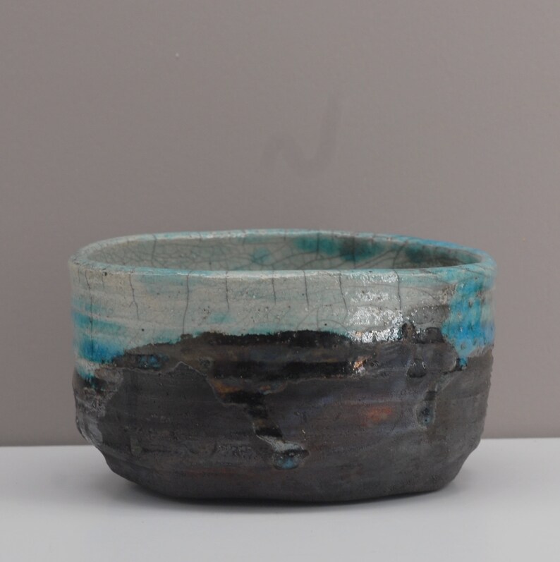 Puede incluir: Un cuenco de cer&aacute;mica con un esmalte blanco y detalles azules y negros. El cuenco tiene un esmalte craquelado y una superficie rugosa y texturizada.