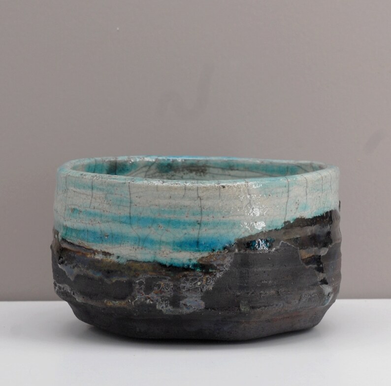 Puede incluir: Un cuenco de cer&aacute;mica con un esmalte azul y blanco y un borde negro. El cuenco tiene un aspecto r&uacute;stico y hecho a mano.