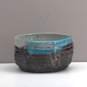 Puede incluir: Un peque&ntilde;o cuenco redondo de cer&aacute;mica con un esmalte craquelado. El cuenco tiene una base marr&oacute;n oscura con un esmalte azul y blanco alrededor del borde.