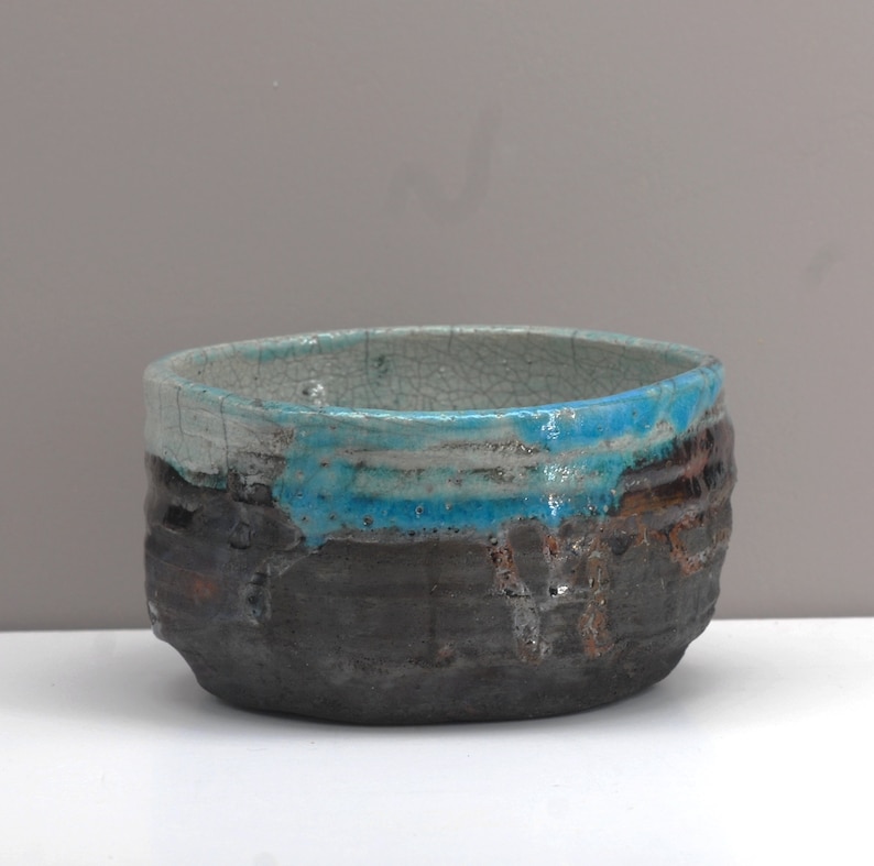 Puede incluir: Un peque&ntilde;o cuenco redondo de cer&aacute;mica con un esmalte craquelado. El cuenco tiene una base marr&oacute;n oscura con un esmalte azul y blanco alrededor del borde.