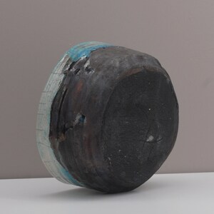 Puede incluir: Un cuenco de cer&aacute;mica negra con un esmalte azul y blanco. El cuenco est&aacute; ligeramente astillado en el borde.