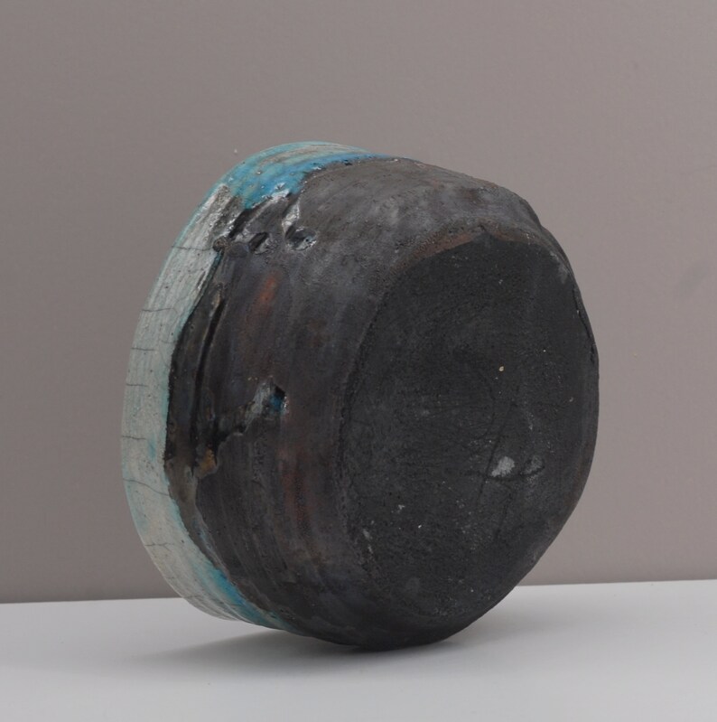 Puede incluir: Un cuenco de cer&aacute;mica negra con un esmalte azul y blanco. El cuenco est&aacute; ligeramente astillado en el borde.