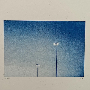 May include: A blue and white print of a night sky with two tall light posts. The print is signed "Cora" and numbered "7/30".