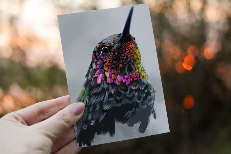 May include: Close-up of a hummingbird with iridescent green, pink, and yellow feathers. The bird's eye is visible, and it is looking up.