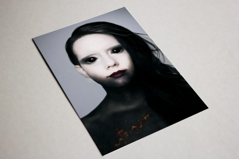 May include: A portrait of a person with pale skin, dark hair, and black eyes. The person's lips are a deep red, and the chest area has a fiery orange design. The background is a light gray.