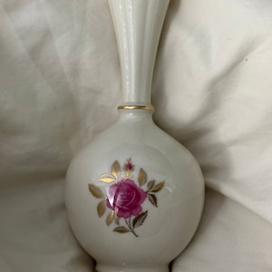 May include: A white porcelain vase with a gold trim and a pink rose with gold leaves design.