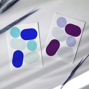 May include: Two cards with abstract shapes in blue, purple, and white. The shapes are reminiscent of pebbles or stones.