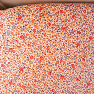 May include: White fabric with a small-scale floral print in shades of orange, yellow, and gray.
