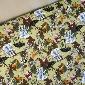 Peut inclure: Tissu vert à motif camouflage représentant divers animaux de la savane, notamment des girafes, des zèbres, des éléphants et des flamants roses. Le tissu porte également l'inscription "Safari".