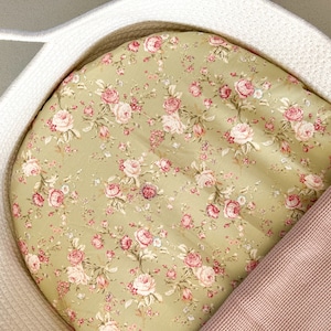Peut inclure: Un panier blanc tissé avec une doublure à motif floral vert et rose et une couverture en tricot rose.