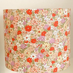 Könnte beinhalten: Ein floral bedruckter Lampenschirm mit weißem Hintergrund und einem Muster aus rosa, roten und gelben Blumen. Der Lampenschirm ist aus Stoff und hat eine zylindrische Form.