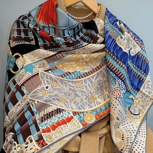 May include: A colorful silk scarf with a geometric pattern in shades of blue, red, brown, and gold. The scarf is draped over a beige coat.